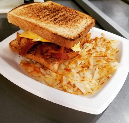 A toasted sandwich with bacon and cheese, served with a side of crispy hash browns on a white plate.