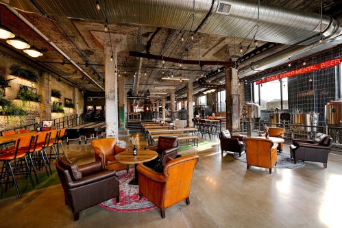 A spacious brewery interior with industrial decor, cozy seating, and brewing equipment in the background.