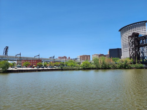 A view of a river with buildings and greenery along the shore under a clear blue sky.
