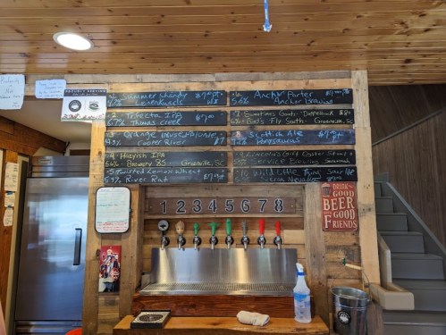 A wooden bar menu displaying various beers on tap with prices, alongside a clean, rustic interior.