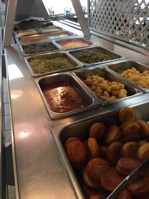 A buffet table with various dishes in metal trays, including greens, cornbread, and sauces.