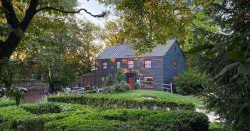 A charming dark blue house with red accents, surrounded by lush greenery and trees in a serene outdoor setting.