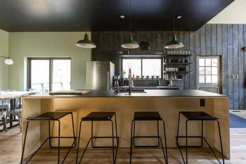 Modern kitchen with a wooden island, black countertops, green pendant lights, and sleek bar stools.