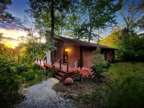 A cozy log cabin surrounded by trees, with a warm glow from the windows at sunset.