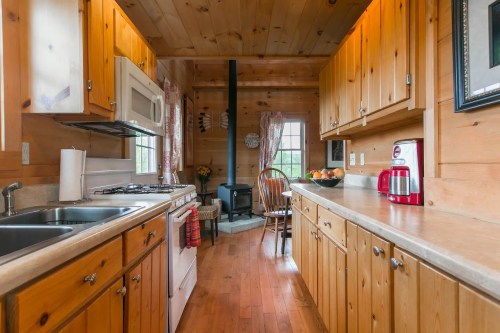 Cozy wooden kitchen with a stove, sink, and dining area, featuring warm tones and natural light.