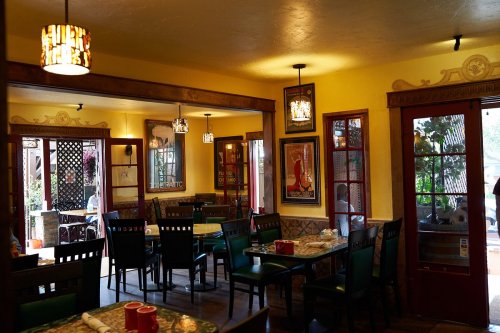 Cozy restaurant interior with colorful walls, wooden furniture, and decorative lighting, featuring empty tables and chairs.