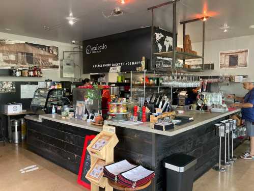 A cozy café interior with a wooden counter, shelves of drinks, and a barista preparing orders.