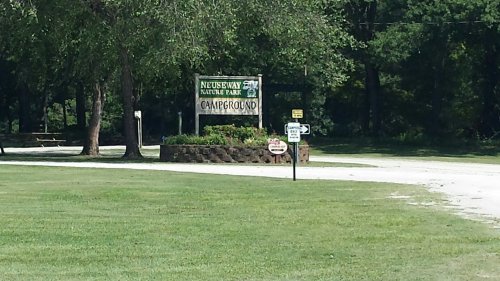 Sign for Neuseway Nature Park Campground, surrounded by trees and grassy area, with a clear blue sky above.