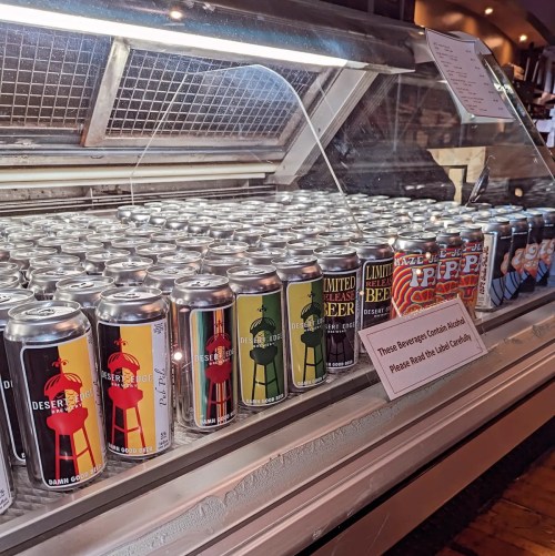 A display case filled with colorful beverage cans, featuring various designs and a sign about alcohol content.