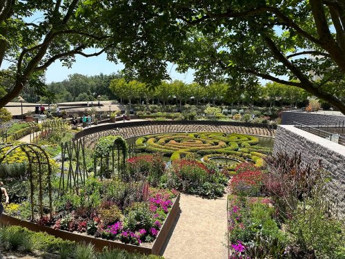 A beautifully landscaped garden featuring a circular maze of greenery surrounded by colorful flowers and trees.