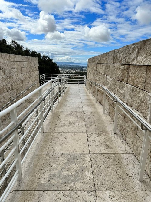 A wide, paved walkway with railings leads towards a scenic view under a partly cloudy sky.