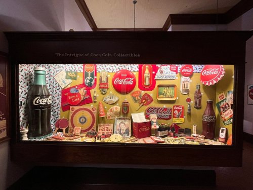 Display case filled with vintage Coca-Cola collectibles, including bottles, cans, and advertising memorabilia.