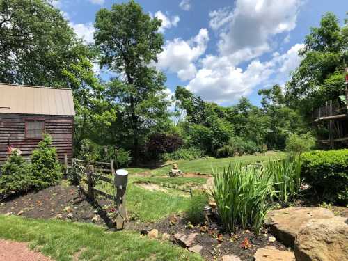 A scenic garden with lush greenery, a wooden shed, and a blue sky dotted with clouds.