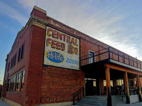 Historic brick building with a faded "Central Feed Co" sign and a modern balcony under a blue sky.