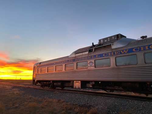 A vintage train car named "Charlie Russell Chew Chew" against a vibrant sunset sky.