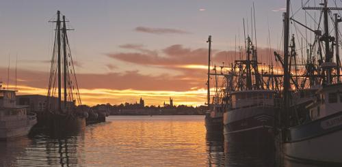 Sunset over a harbor filled with fishing boats, silhouetted against a colorful sky and calm water.