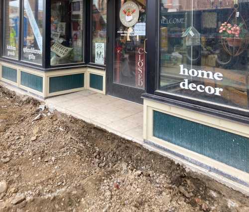 A storefront with a "Closed" sign, featuring a dirt area in front and a tiled walkway leading to the entrance.