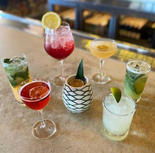 A variety of colorful cocktails arranged on a bar counter, featuring garnishes like lemon and lime.