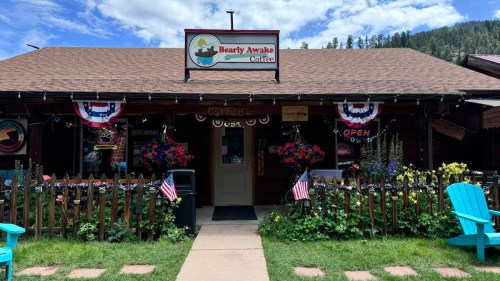 A cozy coffee shop with a sign reading "Bearly Awake Coffee," decorated with flowers and American flags.