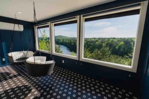 A cozy room with two hanging chairs and large windows overlooking a lush river landscape.