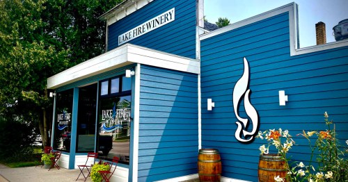Exterior of Lake Fire Winery, featuring a blue facade, large windows, and decorative barrels with flowers in front.