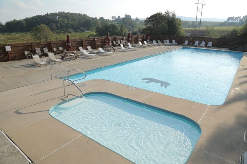 A clear swimming pool with a shallow area, surrounded by lounge chairs and umbrellas, set against a scenic landscape.