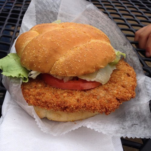 A crispy chicken sandwich with lettuce and tomato on a toasted bun, served on a paper wrapper.