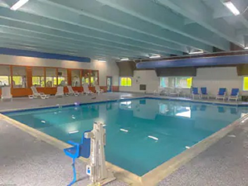 Indoor swimming pool with clear blue water, surrounded by lounge chairs and large windows.