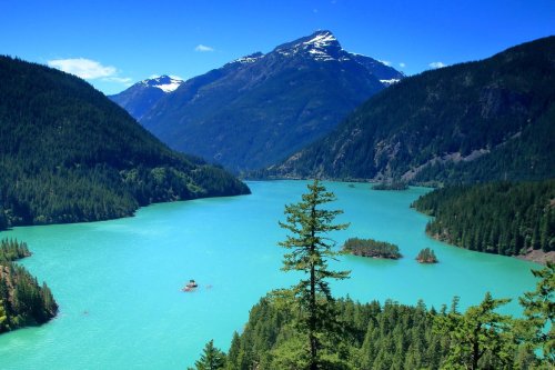 A serene lake surrounded by lush green mountains under a clear blue sky, with small islands dotting the water.