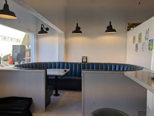 A cozy restaurant booth with blue seating, a small table, and pendant lights, featuring a bright, minimalist design.