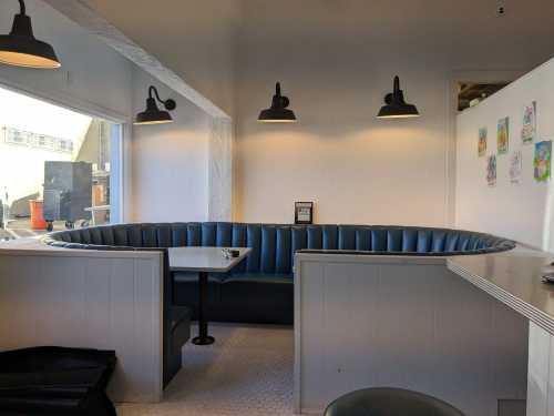 A cozy restaurant booth with blue seating, a small table, and pendant lights, featuring a bright, minimalist design.