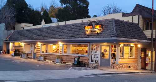 A cozy café with a wooden exterior and a sloped roof, featuring outdoor seating and a warm evening glow.