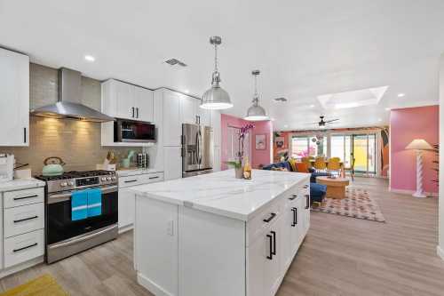 Modern kitchen with white cabinets, stainless steel appliances, and an island, leading to a colorful living area.