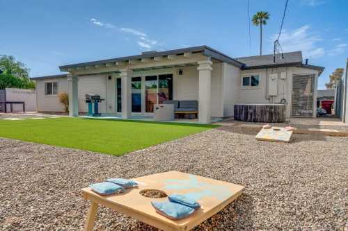 A backyard with a green lawn, cornhole boards, and a modern house featuring a patio and grill.