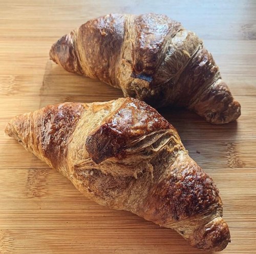 Two golden-brown croissants resting on a wooden surface.