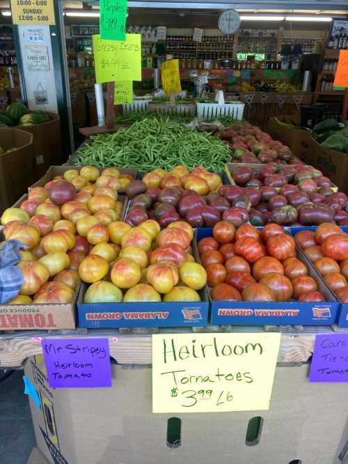 A vibrant market display featuring various heirloom tomatoes and green beans, with colorful price signs.