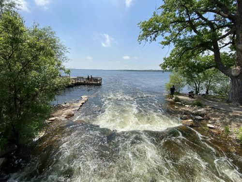 A serene river scene with flowing water, a dock, and trees under a clear blue sky.