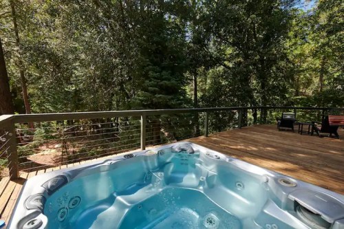 A hot tub on a wooden deck surrounded by lush green trees, offering a serene outdoor retreat.