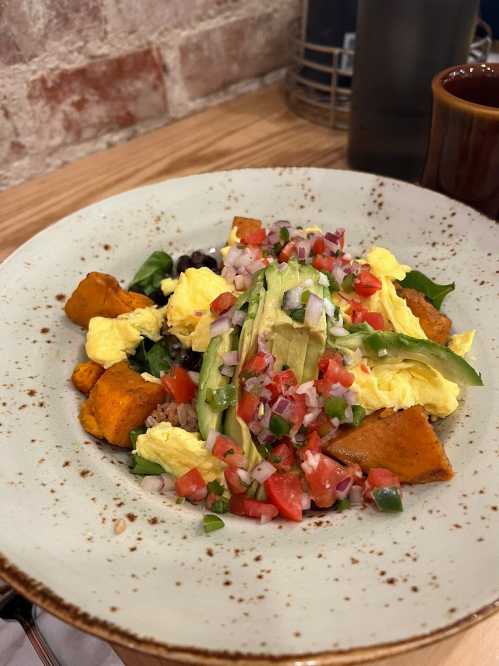 A colorful plate of scrambled eggs, sweet potatoes, black beans, and fresh salsa, garnished with avocado and greens.