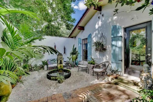 A serene outdoor patio with a fountain, surrounded by lush greenery and cozy seating.