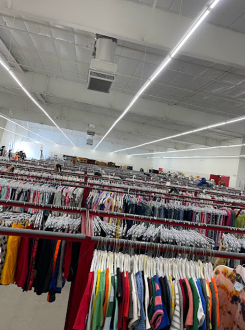 A spacious thrift store filled with rows of clothing on hangers, under bright overhead lights.