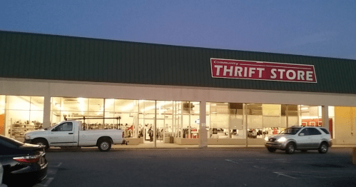 Exterior of a thrift store at dusk, featuring large windows and a sign that reads "Community THRIFT STORE."