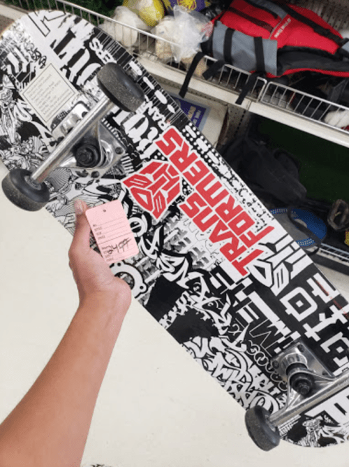 A hand holding a black and white skateboard with various graphic designs and a price tag attached.