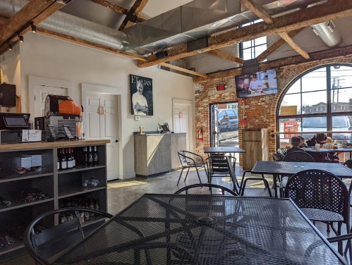 Interior of a cozy café with exposed brick walls, wooden beams, and tables. A counter and a TV are visible.