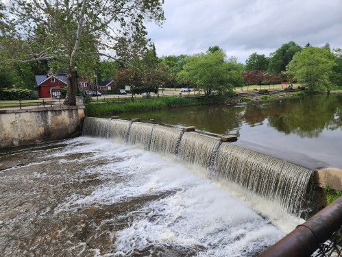 A serene view of a waterfall cascading over a dam, surrounded by greenery and a calm river.