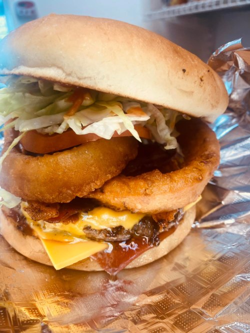 A towering burger with lettuce, tomato, onion rings, cheese, and bacon, served on a toasted bun.
