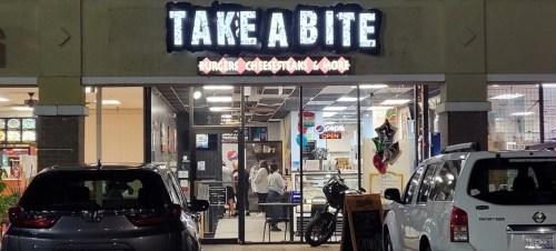 Exterior of "Take A Bite" restaurant, featuring a sign and open door, with cars parked outside.