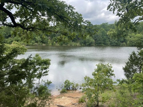 A serene lake surrounded by lush greenery and trees under a cloudy sky.