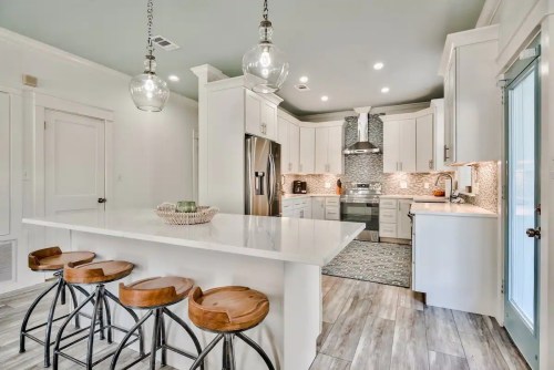 Modern kitchen with white cabinets, a large island, pendant lights, and stylish bar stools. Bright and inviting space.