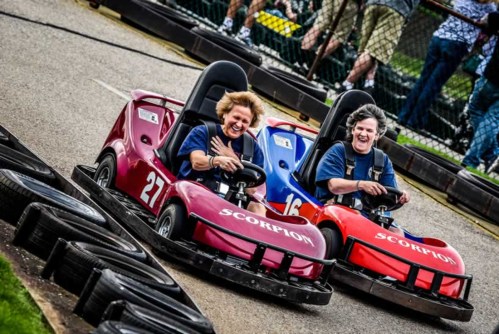 Two people race go-karts on a track, smiling and enjoying the competition. Tires line the course in the background.